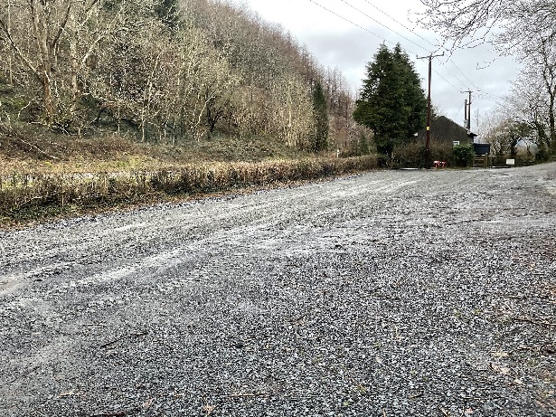 A compacted gravel car park with trees and hills in the background