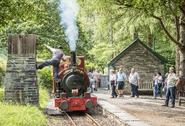 A steam locomotive taking on water as passengers watch from the platform.