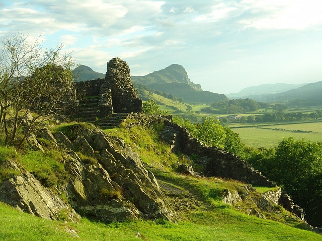 A ruined building with steps leading into it behind jagged rocks. In the distance different mountains can be seen.