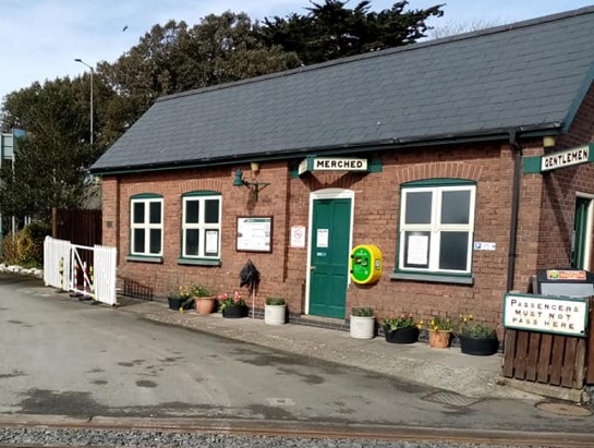A yellow defibrillator mounted to the wall of the slate toilet building.