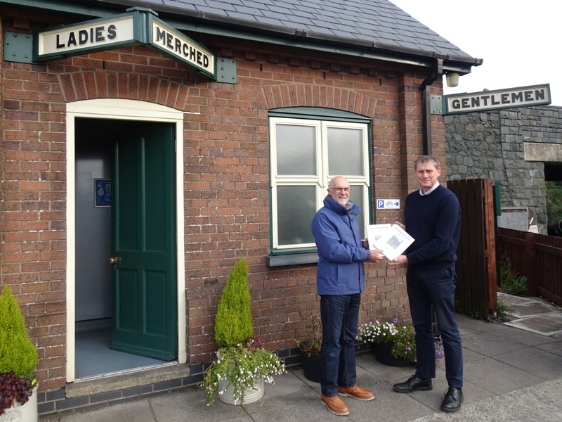 Two people hold certificates outside of the Wharf toilet block