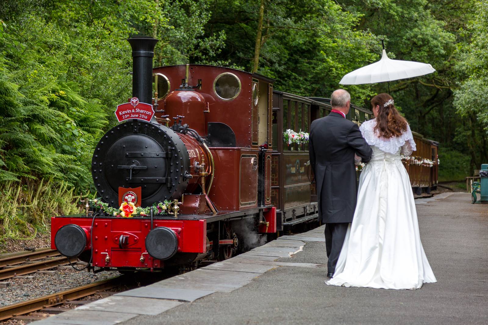 A bride walking along the platform next to a decorated steam train