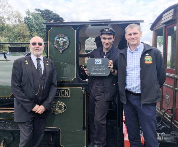 Photograph shows Communications Co-ordinator Lawrence Garvey with Volunteer Co-Ordinator Jack Evans (holding the plaque) and General Manager Stuart Williams.