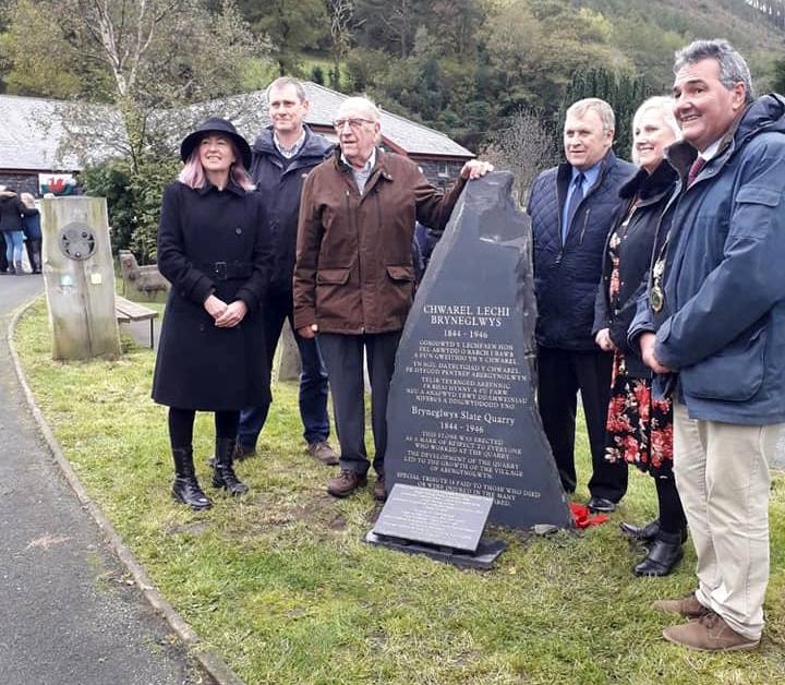 A group of people stood round a slate memorial.