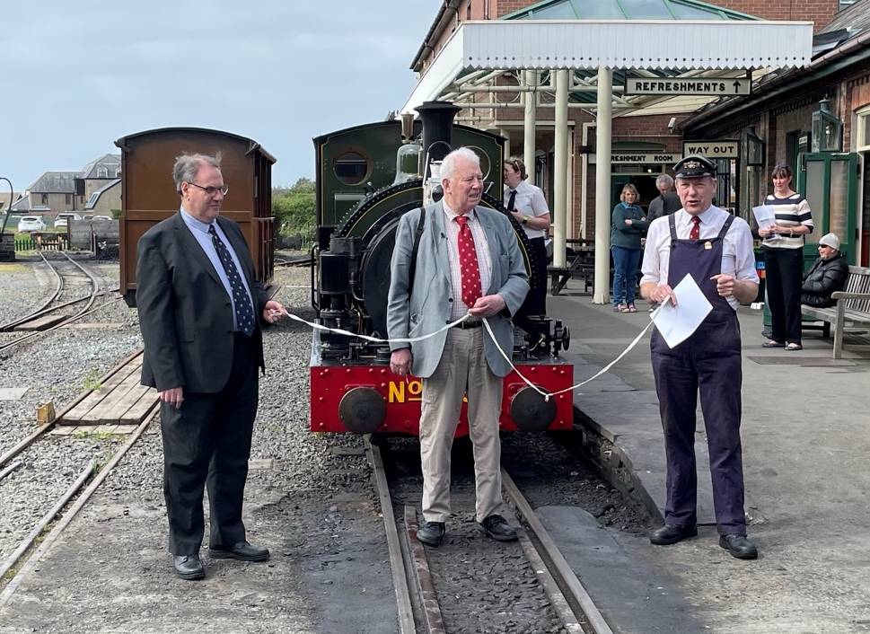 Three men with a white ribbon standing in front of a steam engine