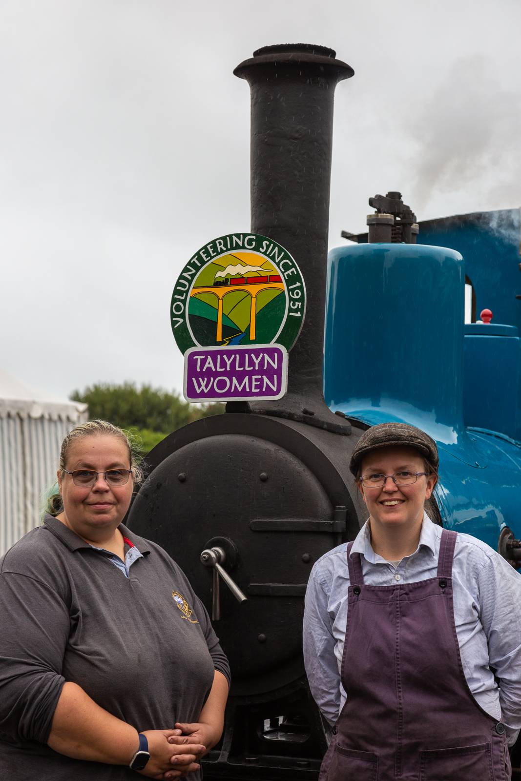 Two women in front of an engine with a headboard.