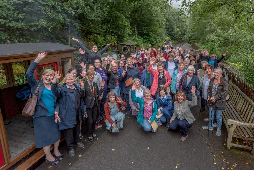 A very large group of women in front of a train.