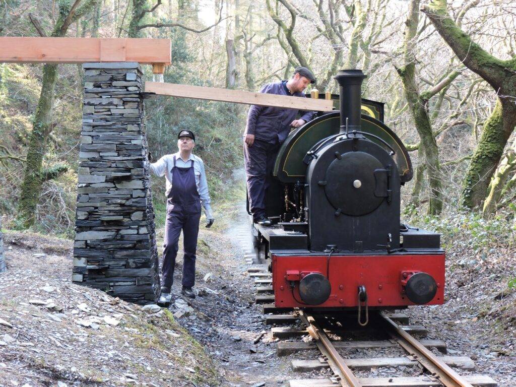 A narrow guage steam engine taking water from a slate water column.
