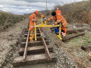 A small, yellow metal crane being used to move rails.