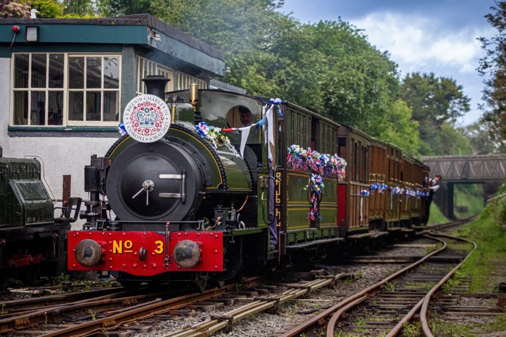 A steam train decortated with red, white and blue ribbons with an intricate headboard.