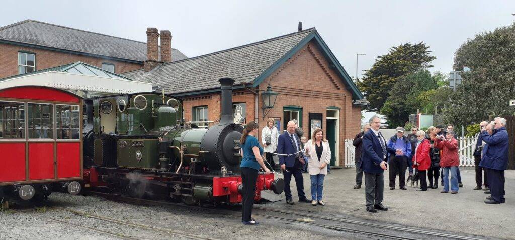 A group of people standing in front of a small green steam locomotive.