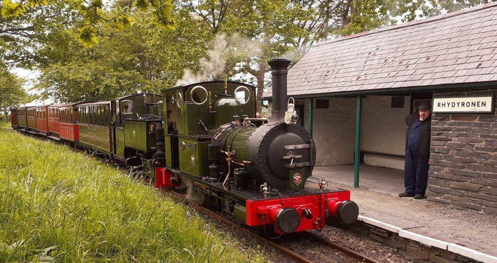 A double-headed narrow guage train at a rural railway station.