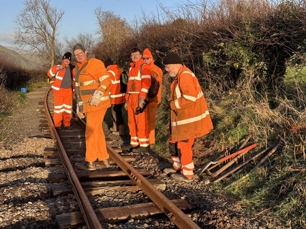 A group of people in orange wor clothes working on railway track.