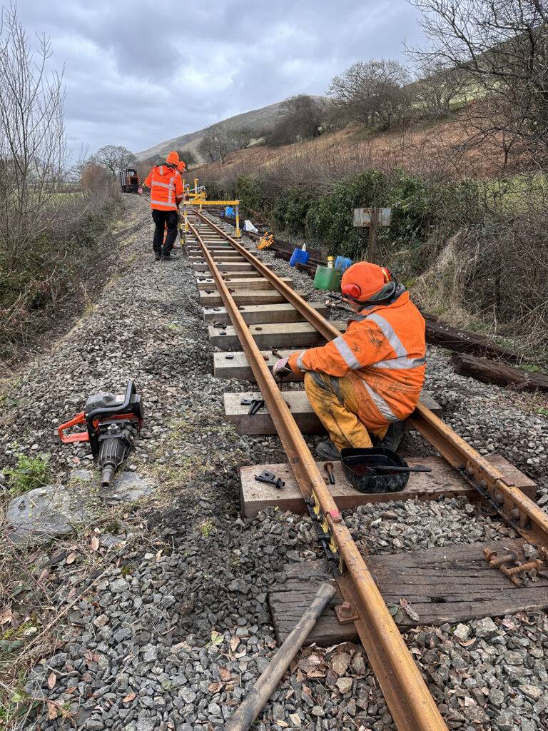 A group of people in orange wor clothes working on railway track.