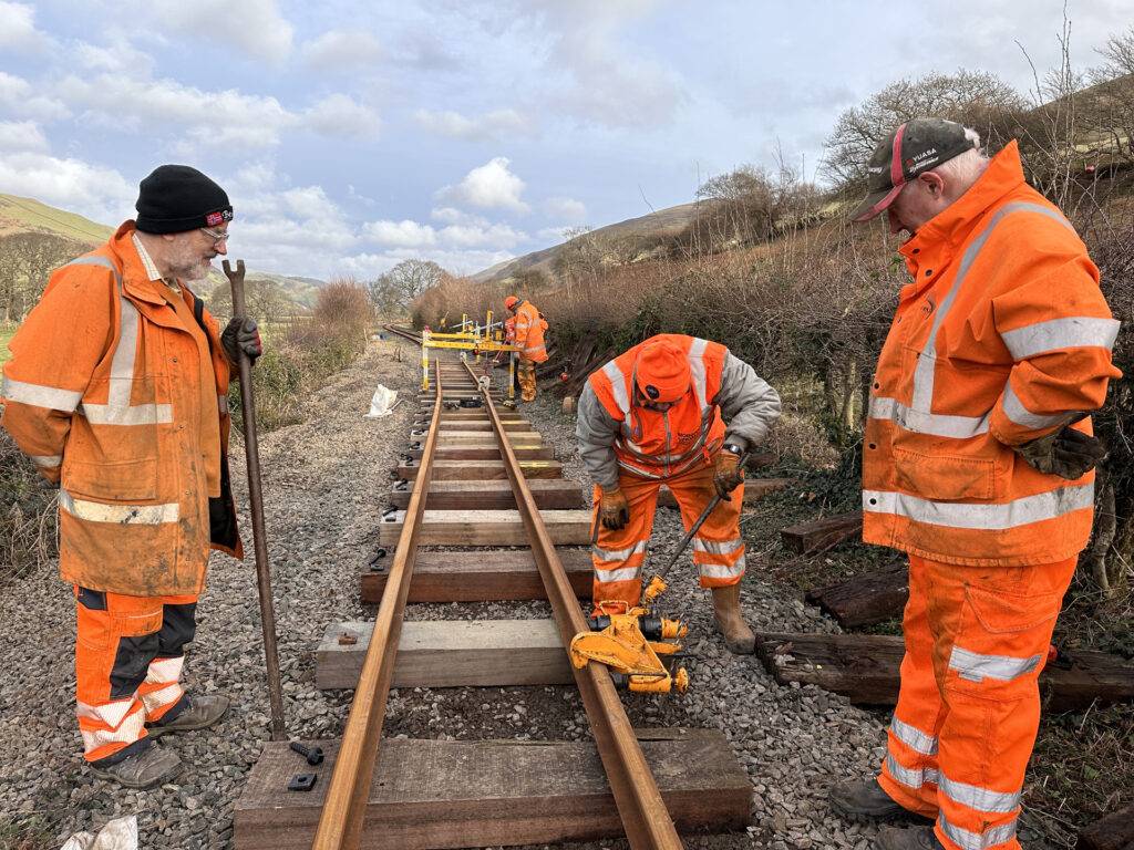 A group of people in orange wor clothes working on railway track.